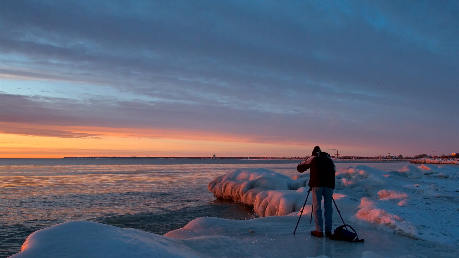 Photographer with a tripod on an icy shore at dawn